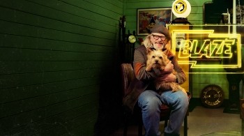 Key art for Junk and Disorderly on Blaze shows host Henry Cole holding a dog, whilst sitting in a shed filled with junk