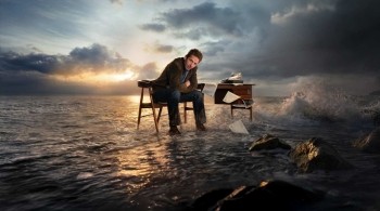 Jim Bergerac sits at a desk surrounded by crashing waves and stormy skies, symbolising inner conflict in the crime drama Bergerac.