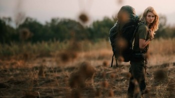 Traveller wearing outdoor clothing and a large hiking backpack walking through dry African grassland during a wilderness expedition