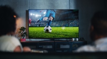 Image shows two people watching a football match on TV