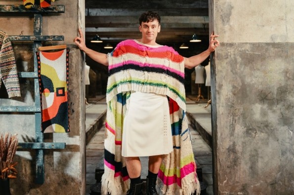 Tom Daley stood in a doorway wearing a woollen jumper and skirt in the show A Game of Wool