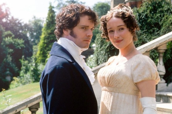 Still image from the 1995 TV series Pride & Prejudice showing a man and woman in Regency-era dress standing on stone steps outdoors, with trees and a country garden behind them.