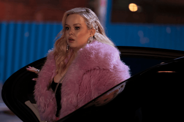 Person in a pink faux‑fur coat stepping out of a car at night, illuminated by street lighting.