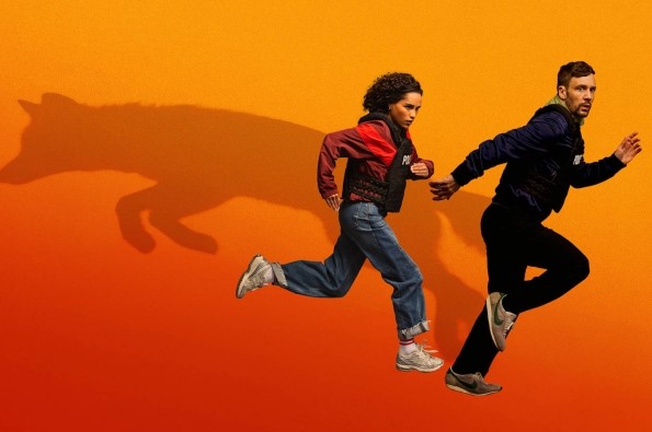 Nick Blood and Saffron Hocking as Leo and Bell in UKTVs new drama Hit Point. A man and woman in casual clothing running against an orange background with the shadow of a dog coming off them.
