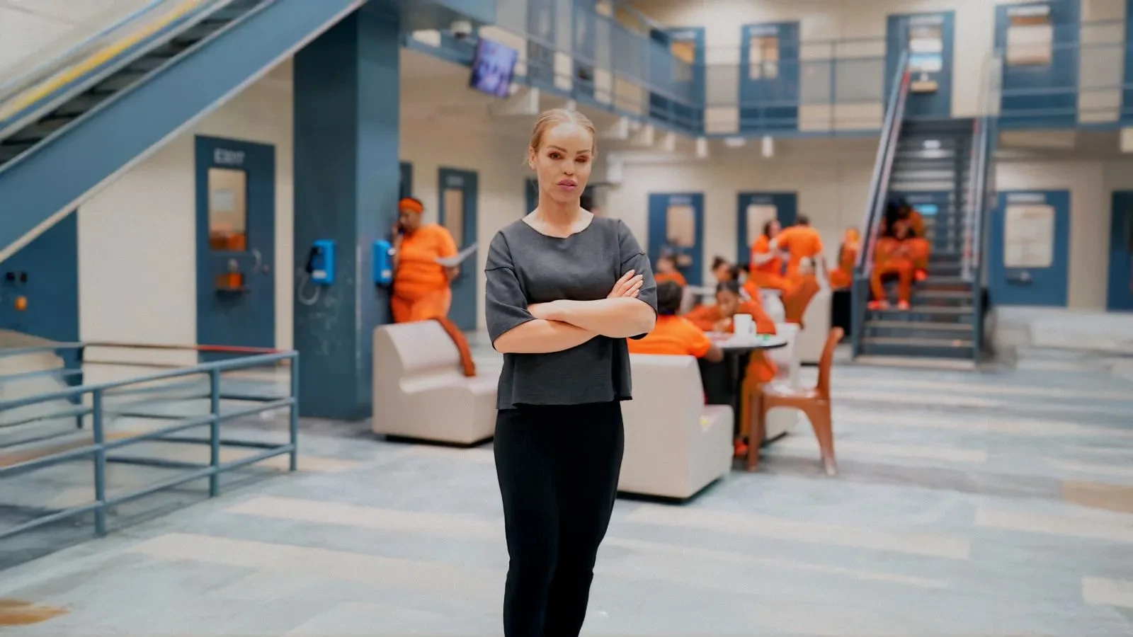 Katie Piper Stood in a prison with inmates in orange jumpsuits in the background