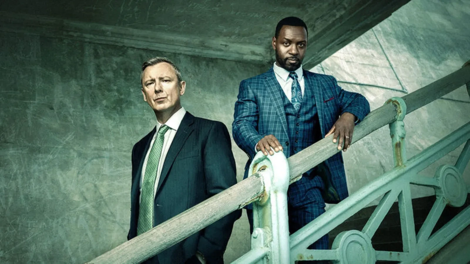 Two men stood on a staircase wearing suits and with serious expressions