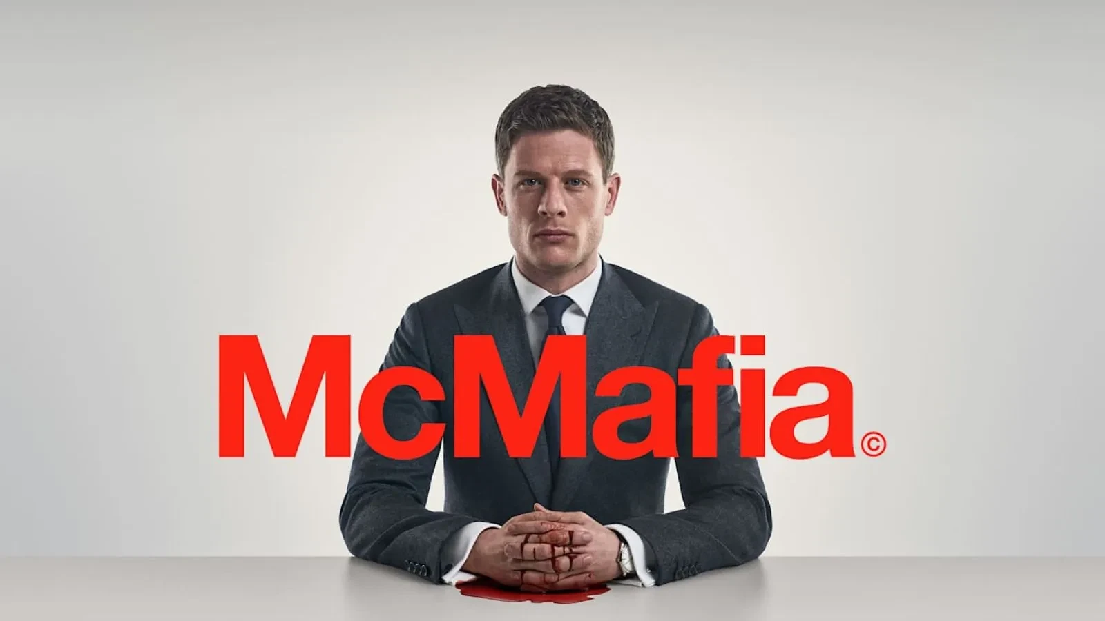 A man in a suite sat at a white table with a white background. Text on top on red that reads McMafia