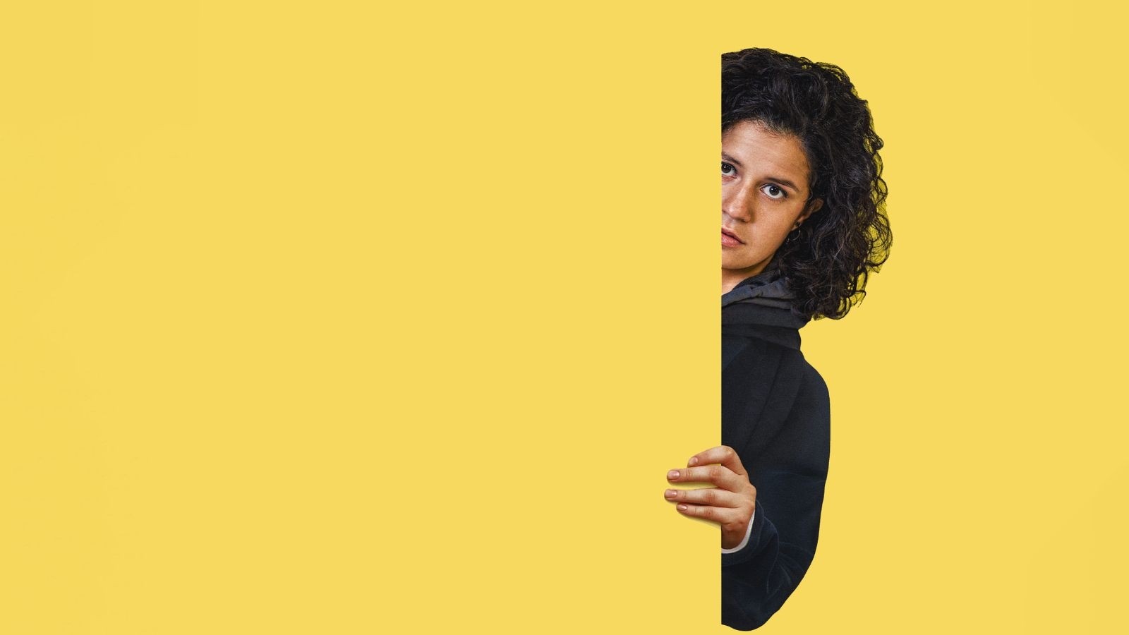 A women peering out behind a yellow background