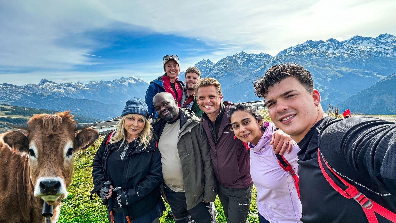 7 celebrities stood with a cow against the backdrop of the alps