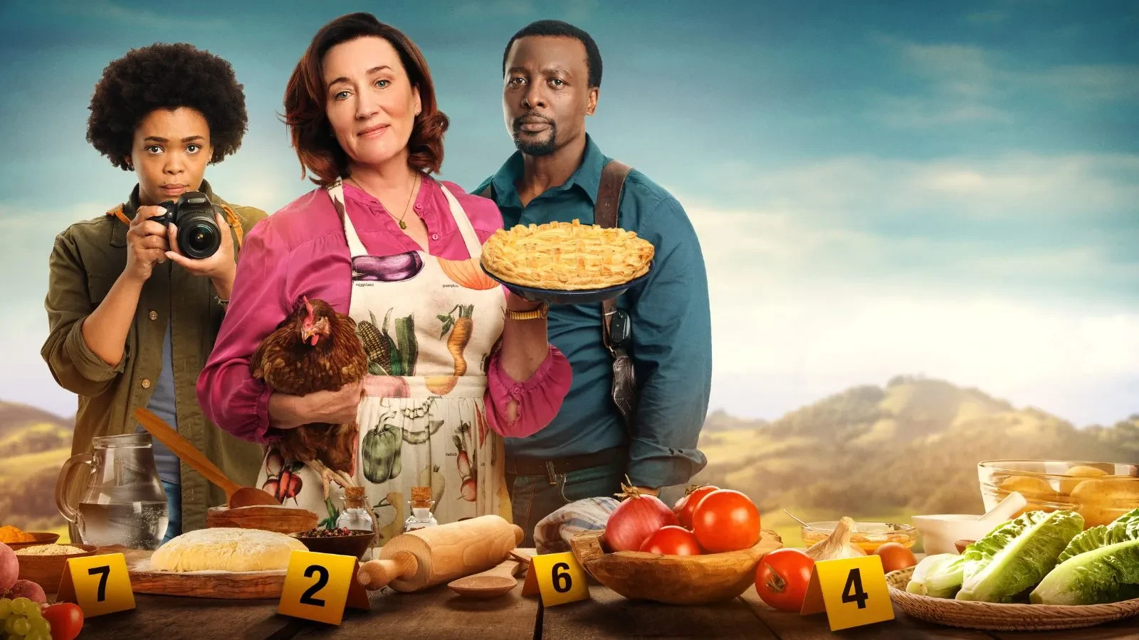 A women holding a pie and a chicken with a women behind her holding a camera and a man to her right staring.