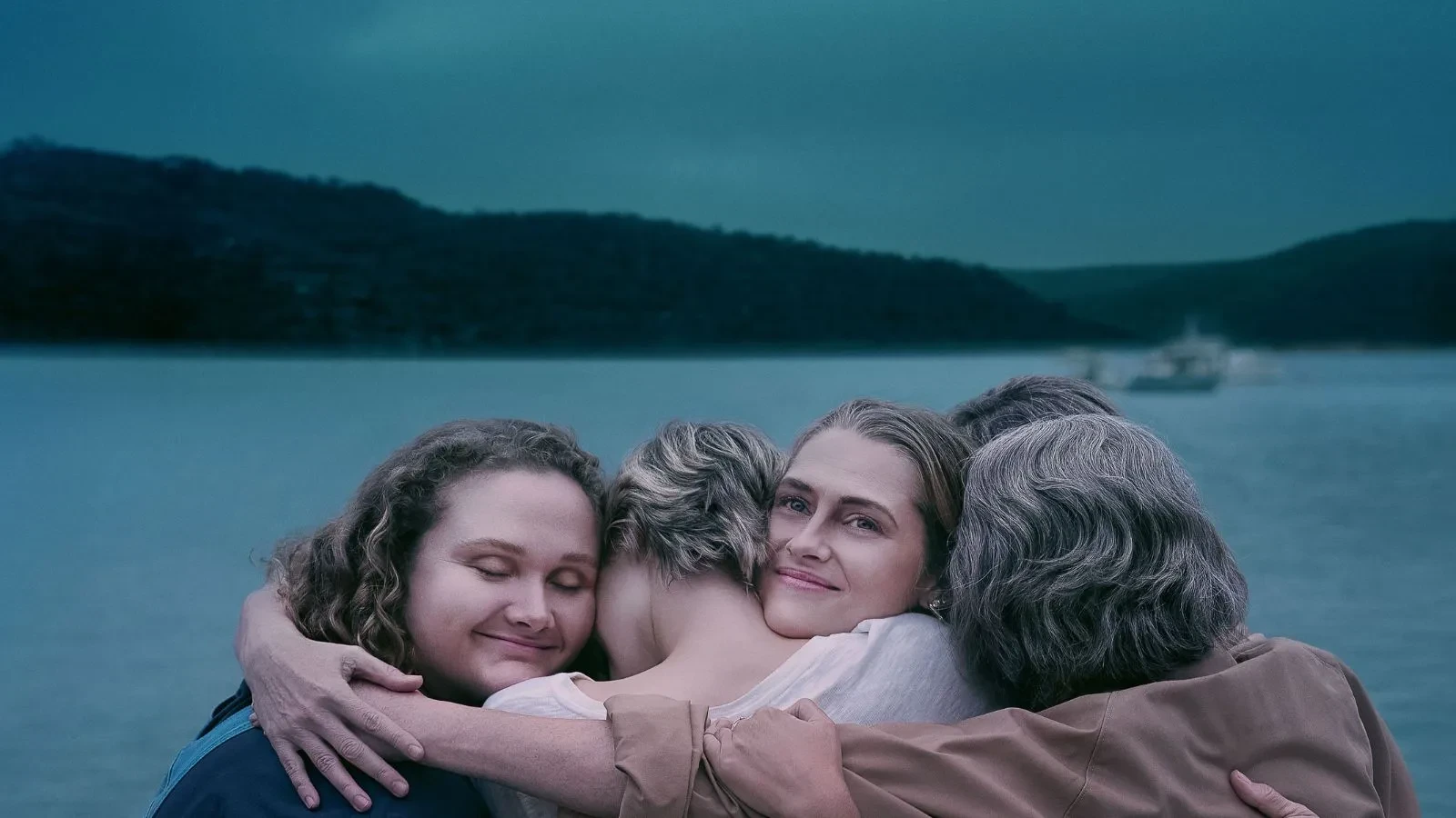 Four young women hugging with a lake in the background