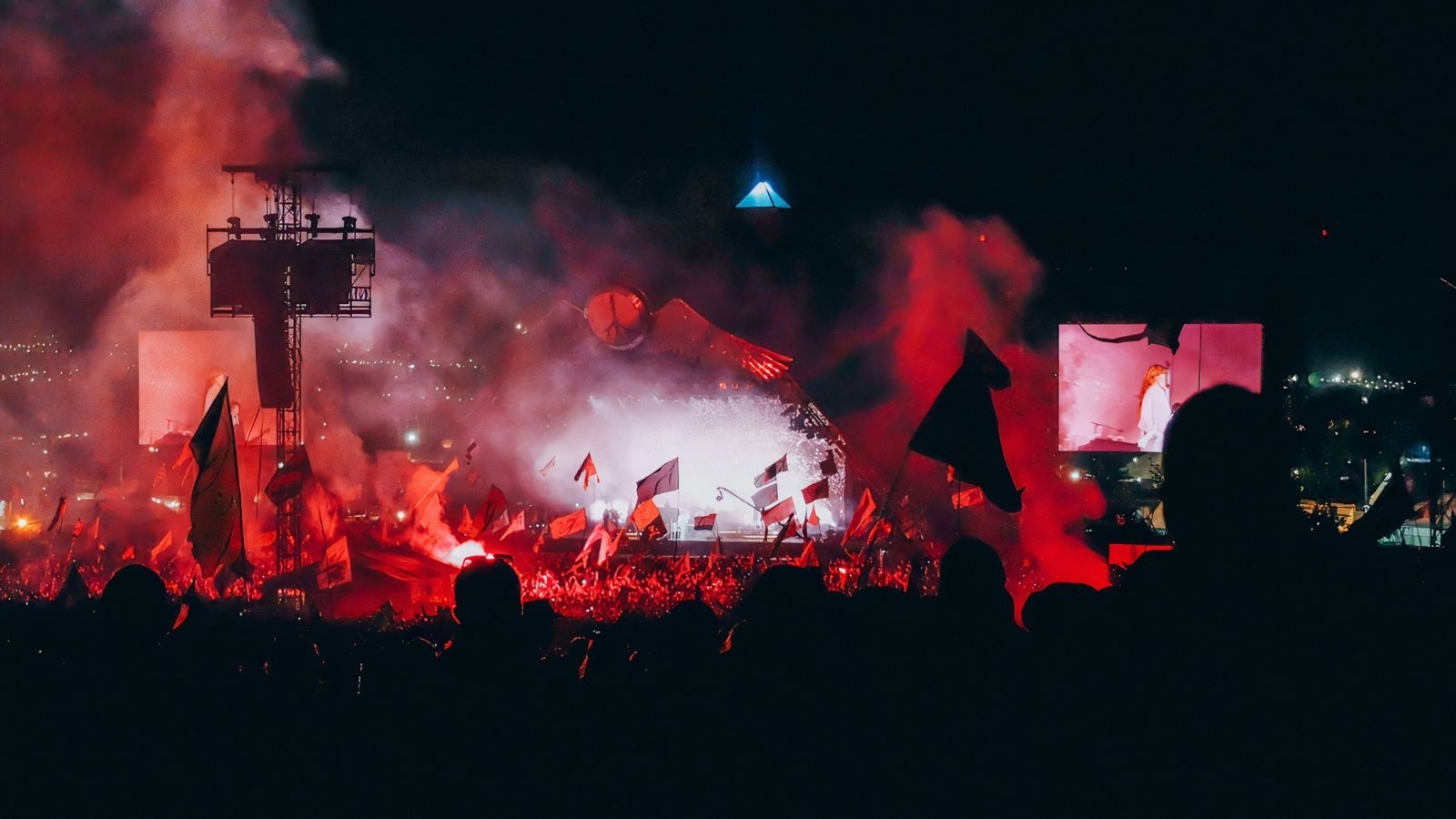 Image of a festival stage surrounded by smoke, crowds and red lights
