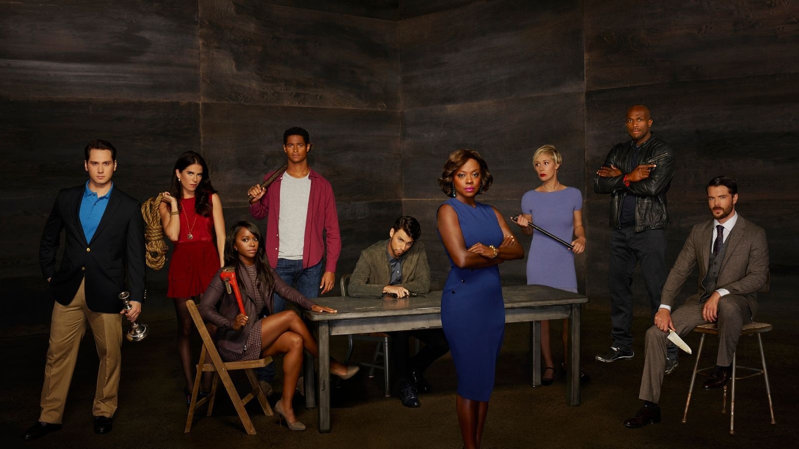 A group of young people stood around a silver table hlding various weapons with an older women in a blue dress stood in front with her arms crossed