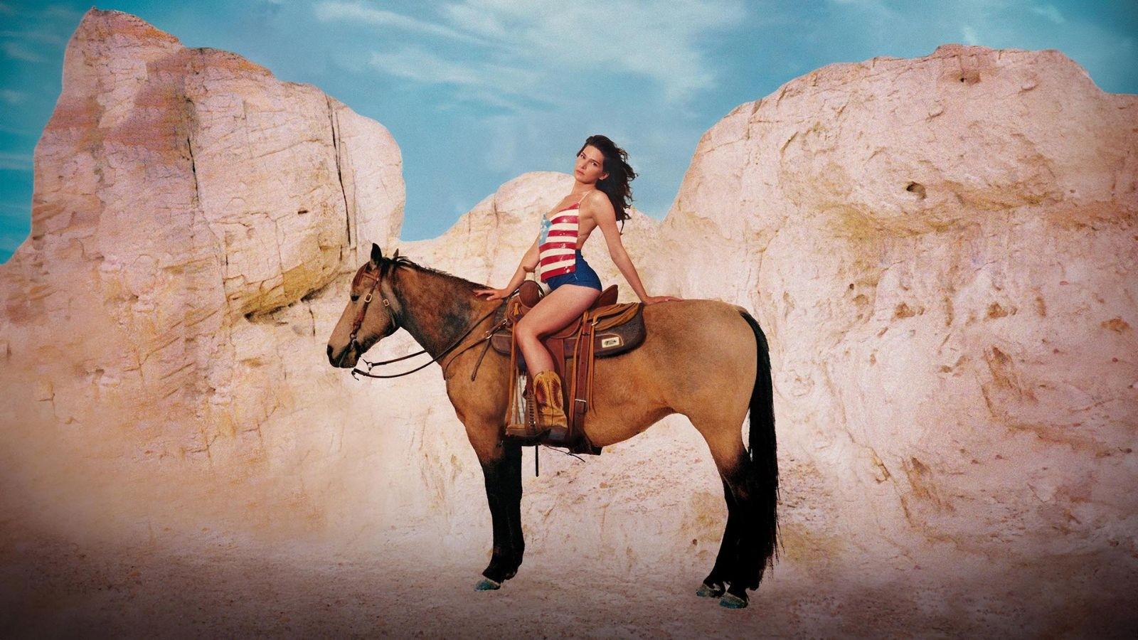 A women in a bikini sat on a brown horse with pink clouds in the background