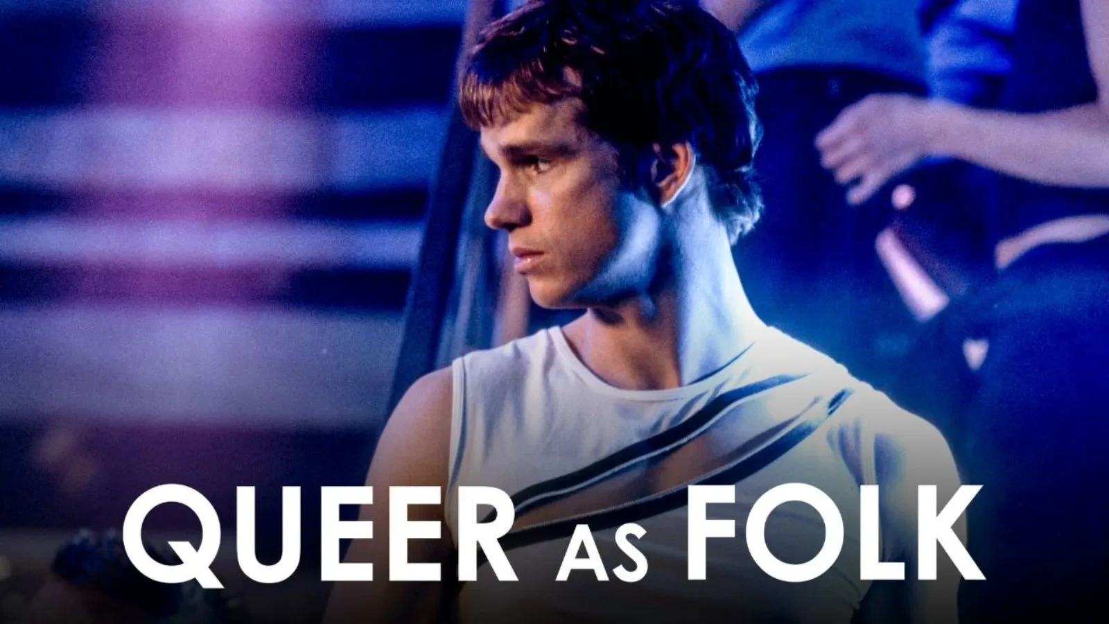 A man in a white vest top stood by a staircase with purple lighting and text that reads queer as folk