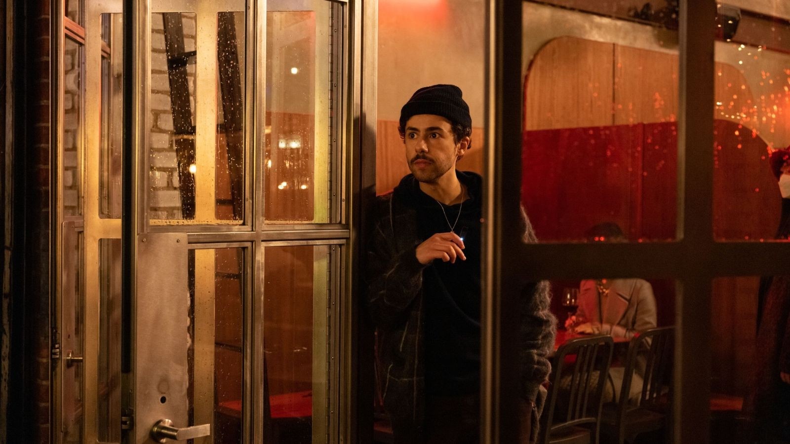 Man with a black beanie on stood just inside a restaurant with the door open looking out
