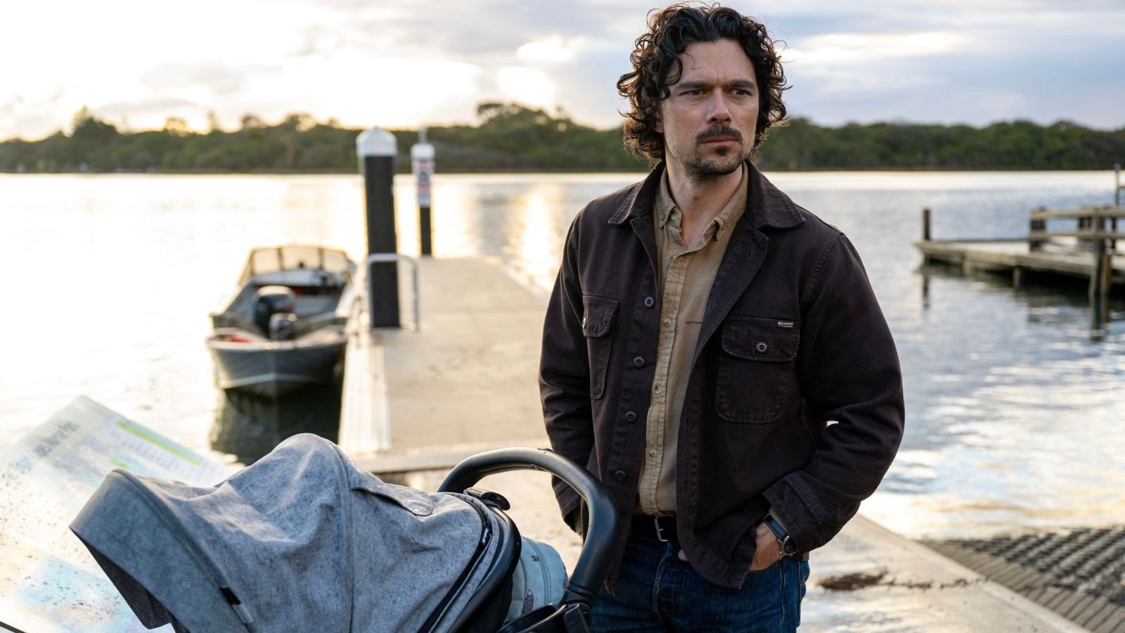 A man with curly hair stood on a pontoon with a pram
