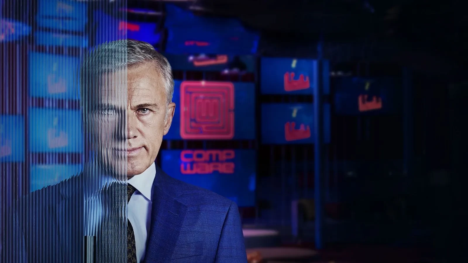 A man stood with half his face behind glass in a room with blue screens