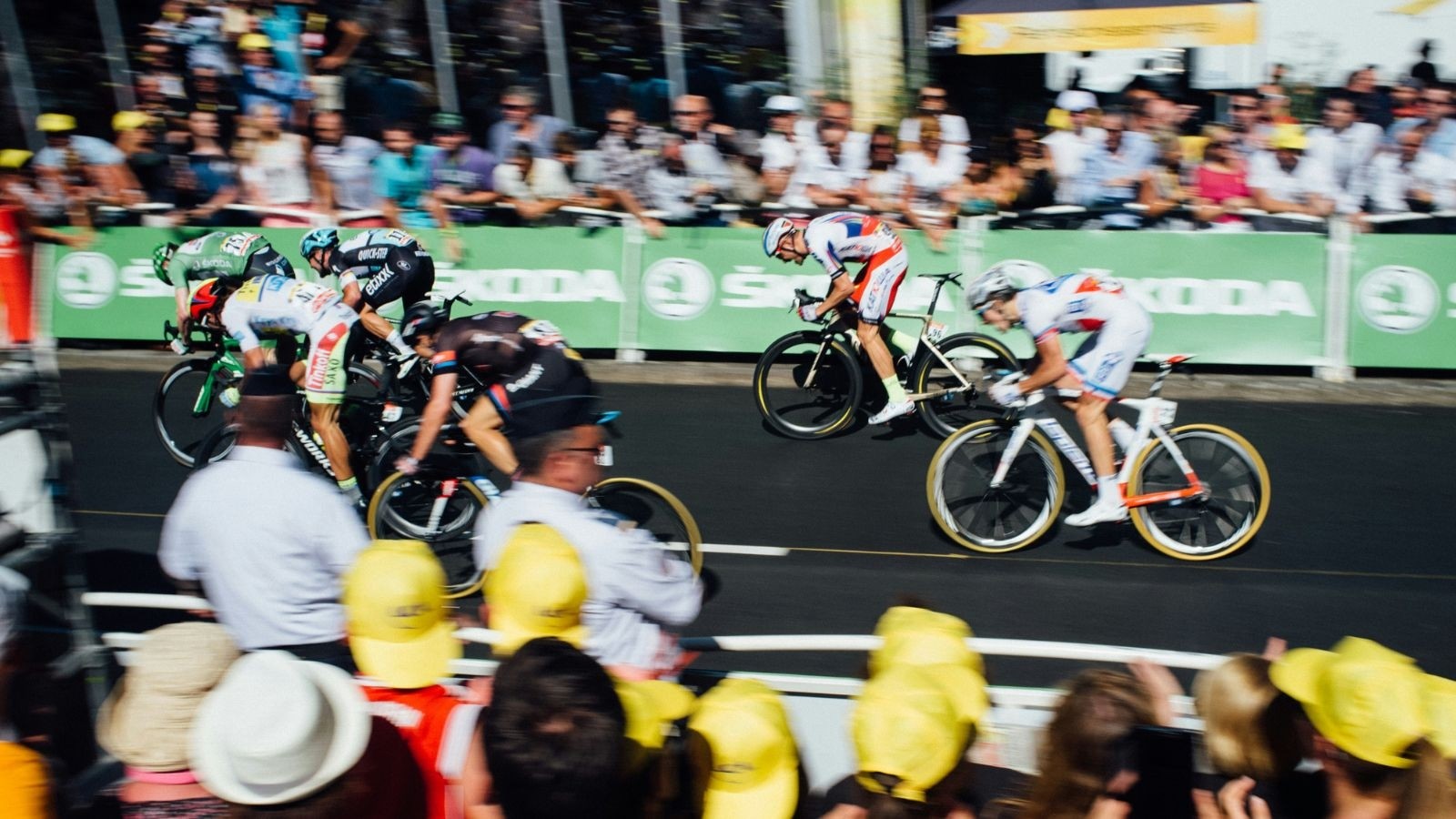 6 cyclists on road bikes cycling past a green banner with people cheering