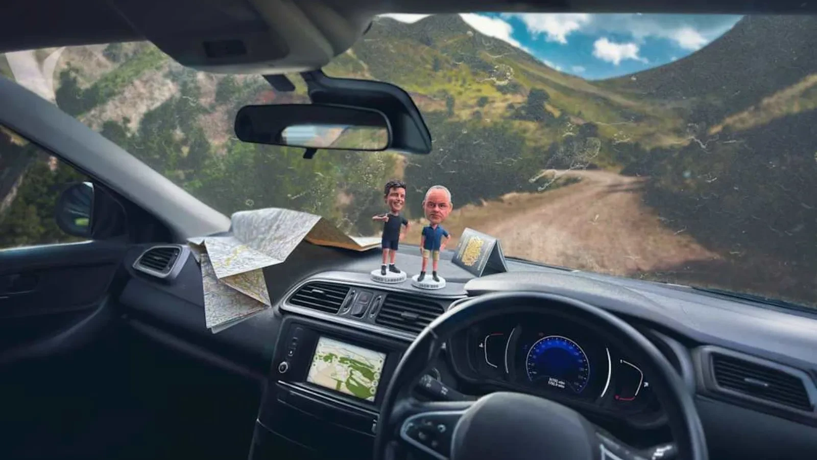 A dashboard of a car with two figures on a road surrounded by mountains