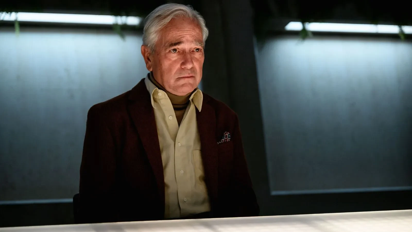 A well dressed man stood in a dimly lit room looking guilty