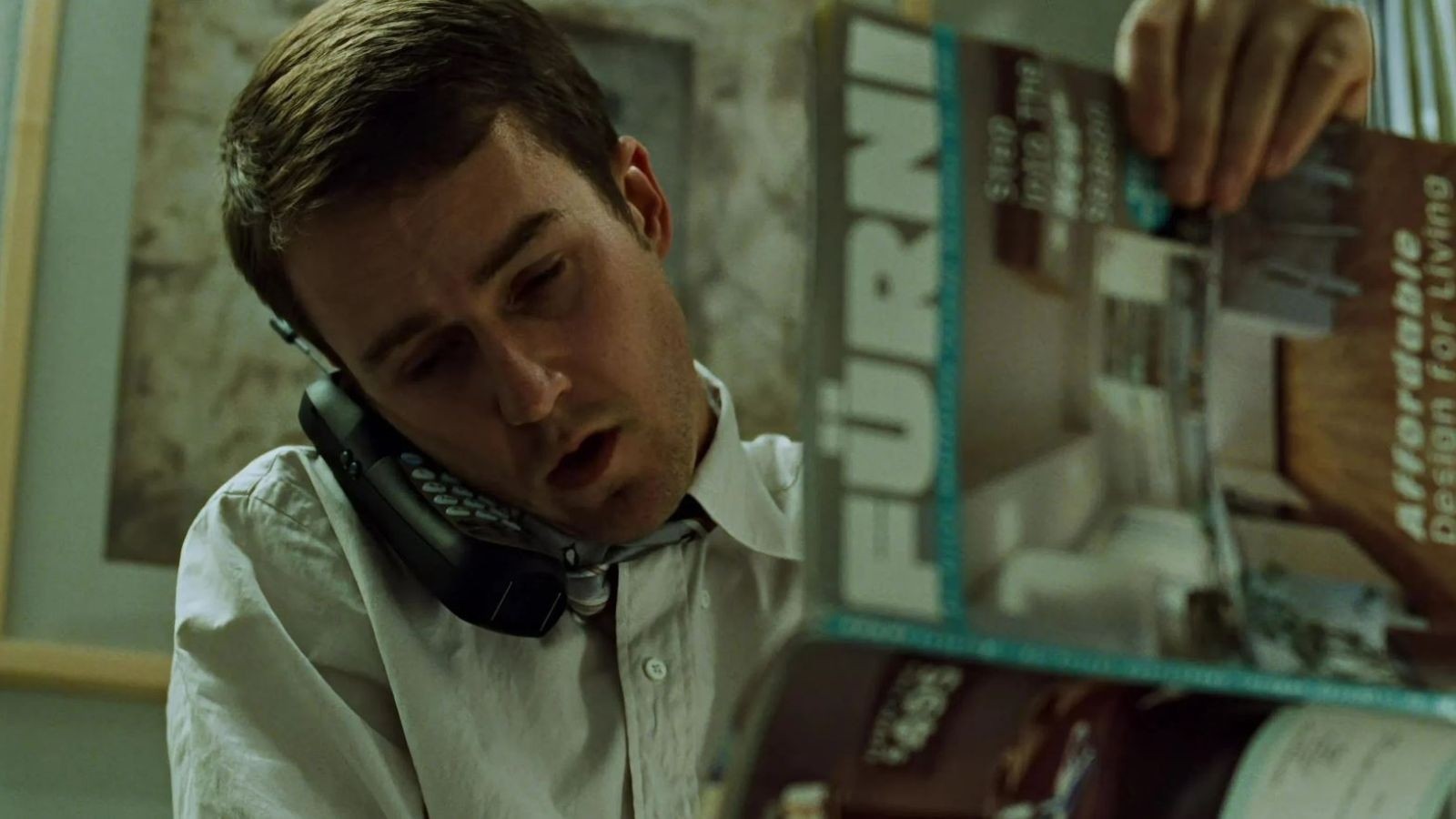 Man with a phone against his head reading a magazine in the movie fight club