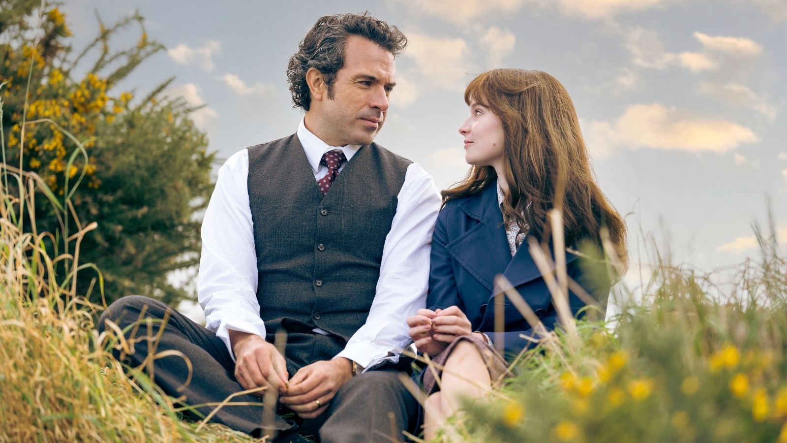 Trespasses first look imagery: A middle aged man and young women staring longingly at each other sat in grass on a sunny day