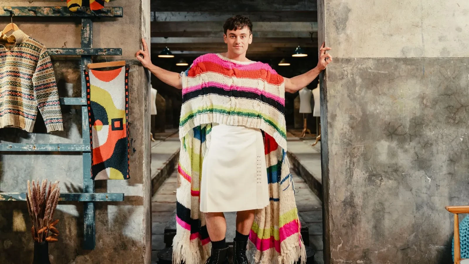 Tom Daley stood in a doorway wearing a woollen jumper and skirt in the show A Game of Wool