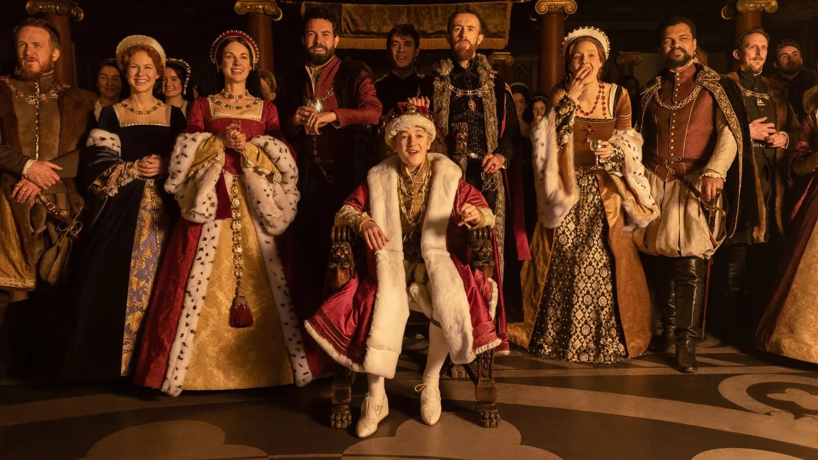 Men and woman dressed in 16th century British Royal clothing laughing in a throne room in the drama Becoming Elizabeth