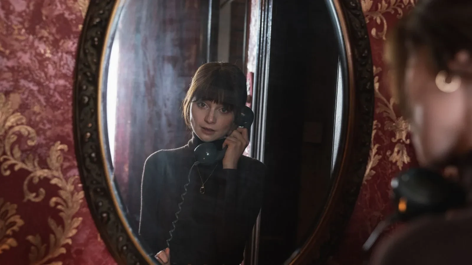 Lola Petticrew with an old fashioned telephone in her right hand looking in the mirror at herself in the drama Trespasses