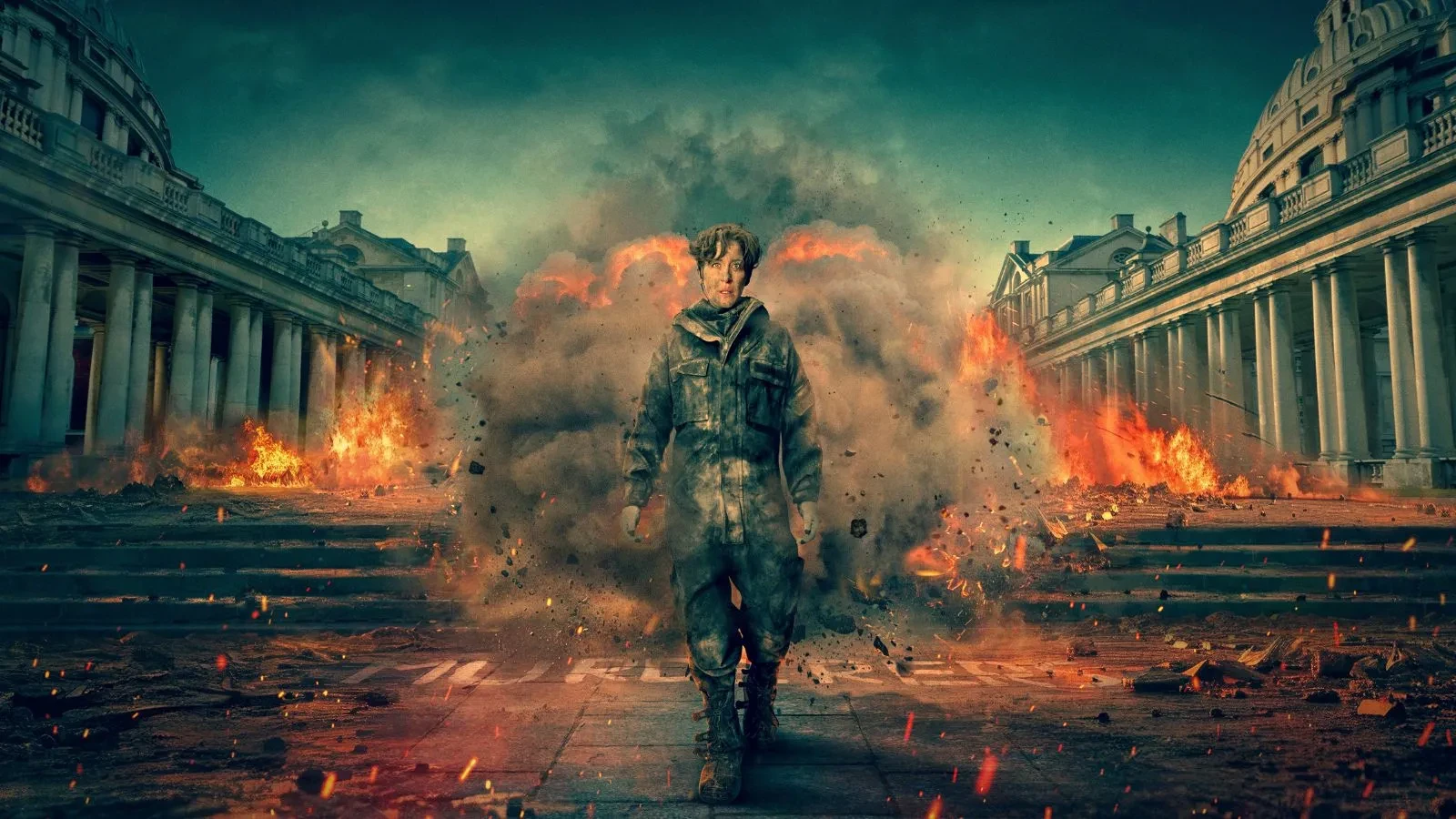 Vicky McClure wearing bomb disposal clothing walking in front of an old building with an explosion behind her
