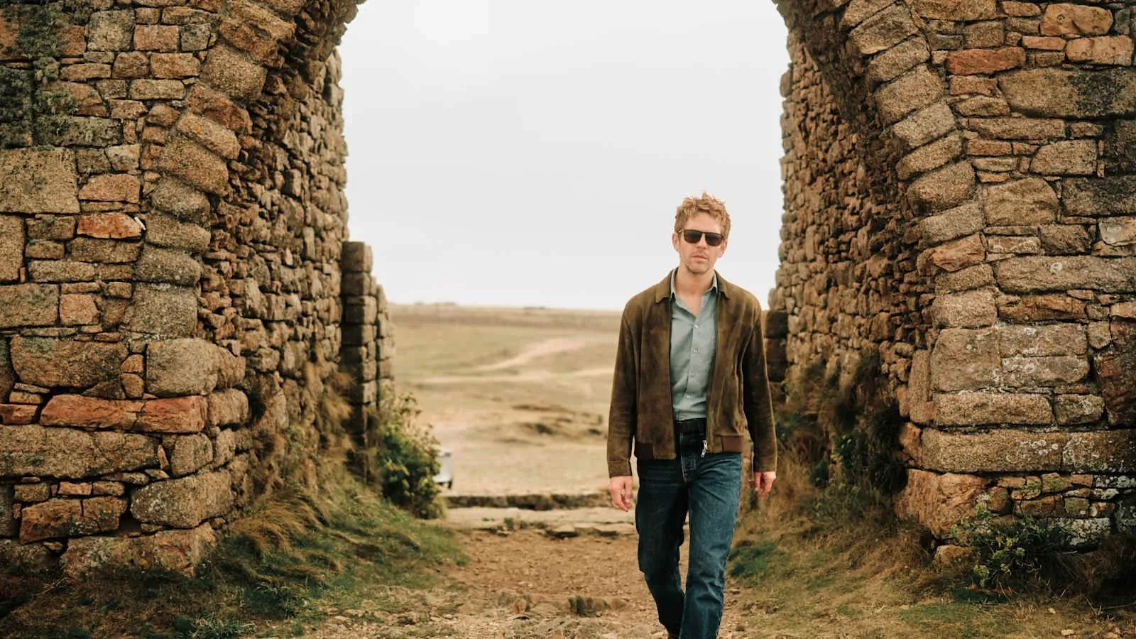 Person walking through a historic stone archway in a rugged outdoor landscape.