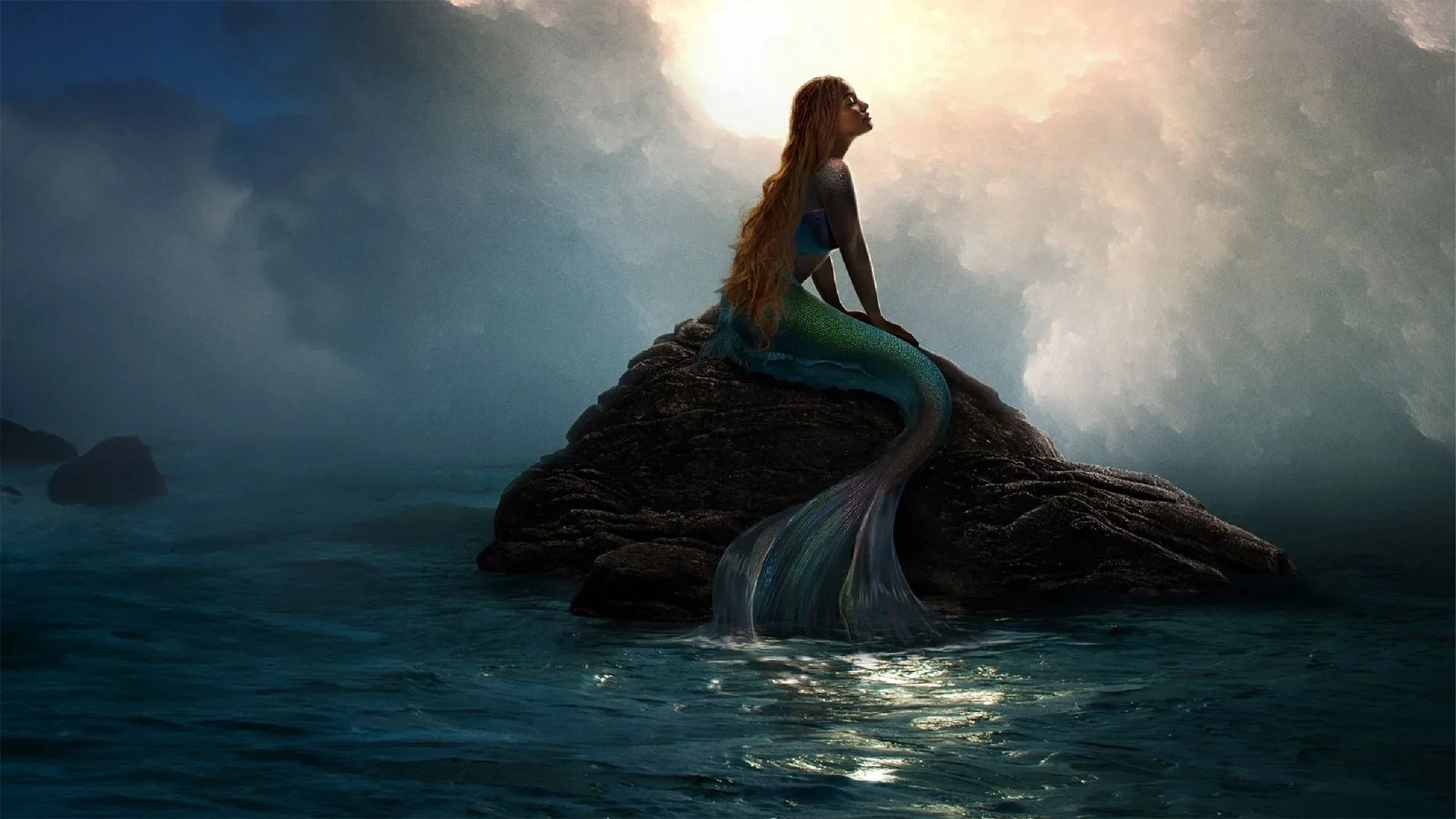Promotional art for the film The Little Mermaid (2023), showing a mermaid with a shimmering tail sitting on a rock in the ocean under a glowing sky.