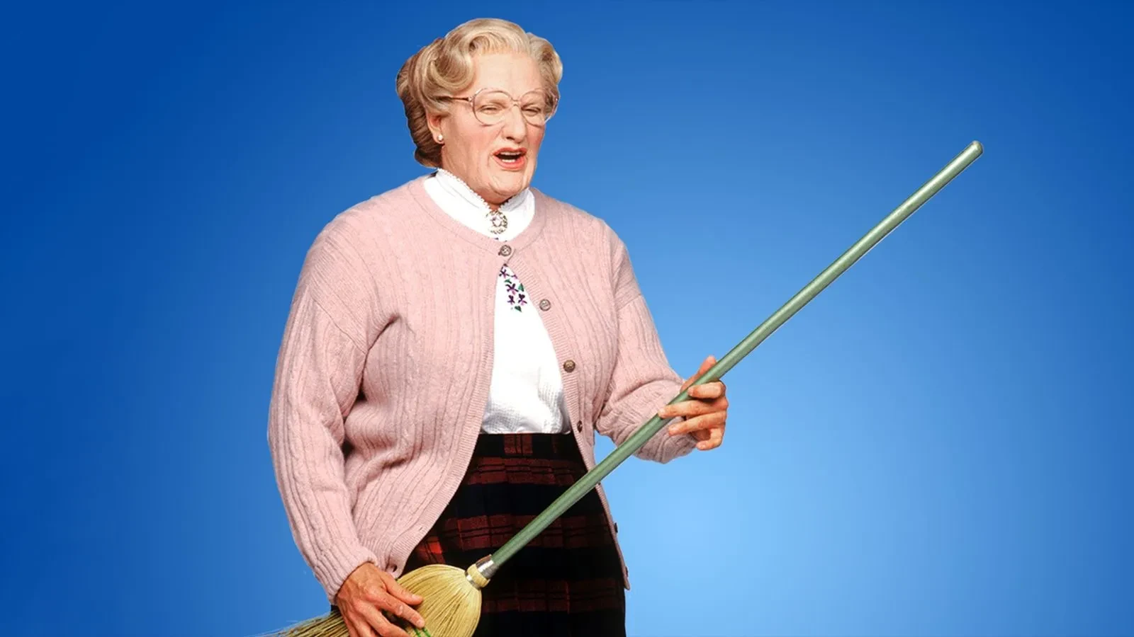 Person wearing a pink cardigan over a white blouse and a tartan skirt, holding a broom against a plain blue background.