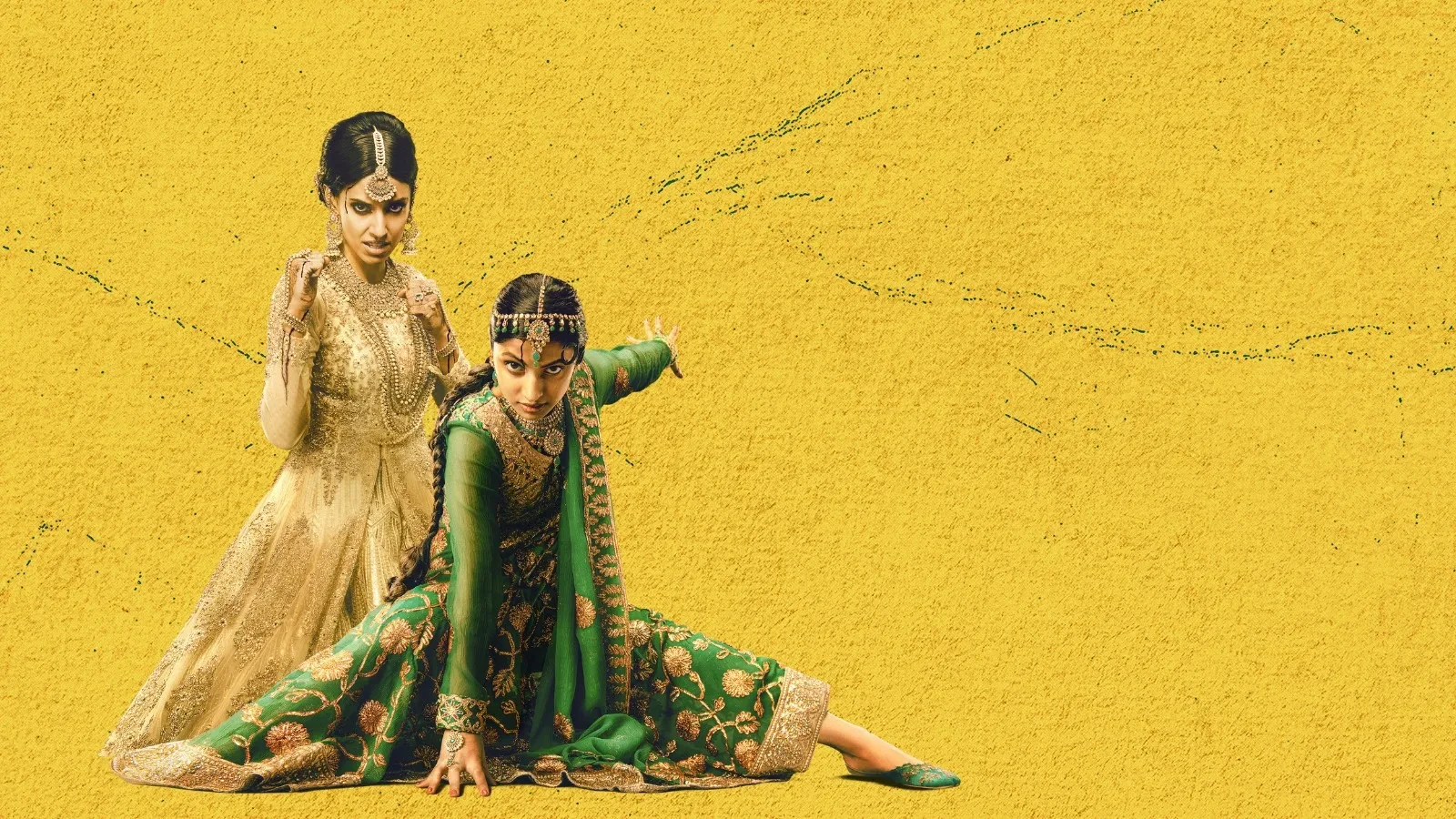 Two women in ornate South Asian attire posed against a bright yellow textured background, one wearing an elegant cream and gold embroidered dress and the other in an intricately patterned green outfit, striking dynamic, expressive martial arts‑inspired poses.