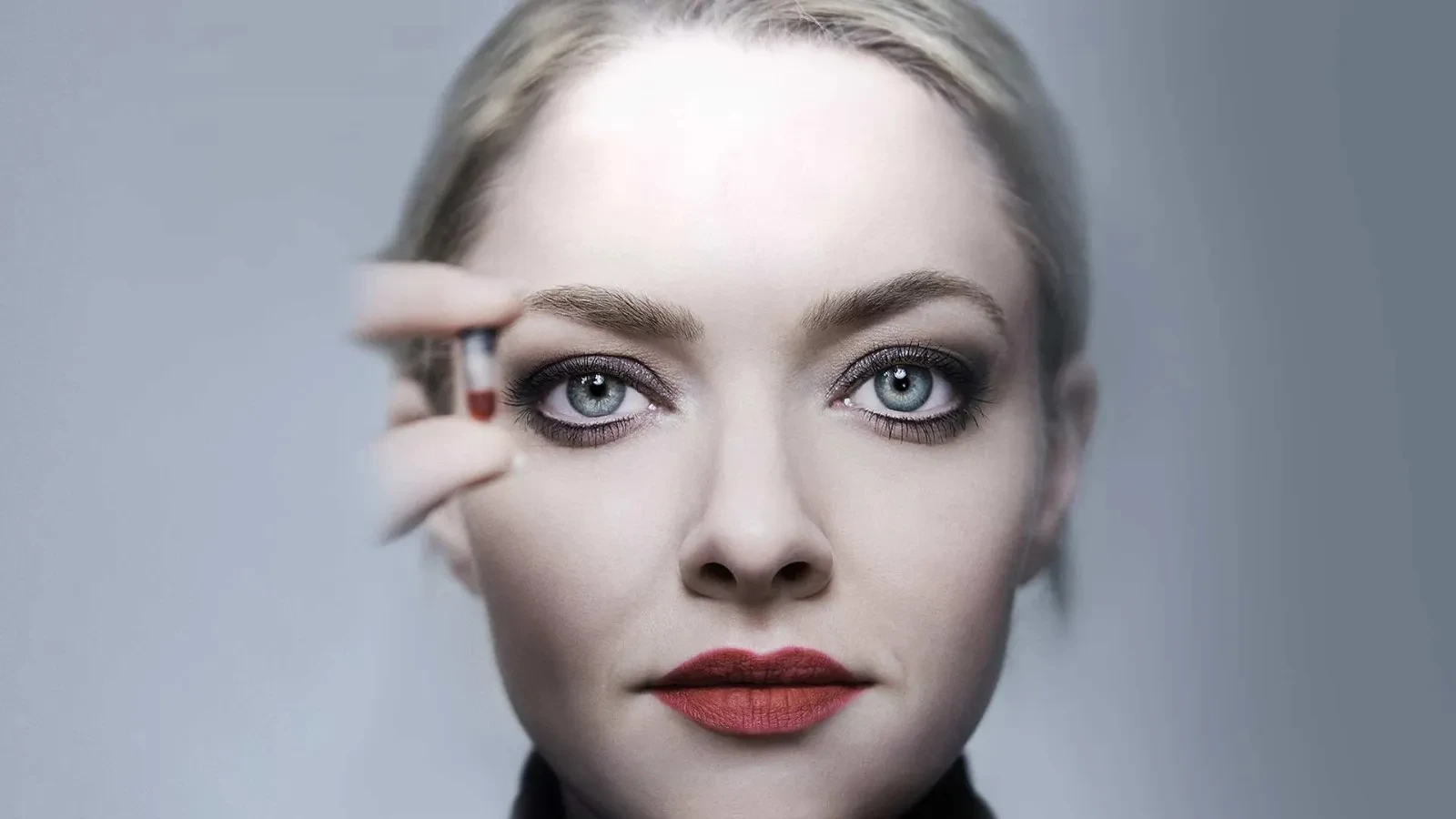 A close‑up portrait composition with a hand gently touching blonde hair against a soft grey background, creating a minimalist and atmospheric visual style.