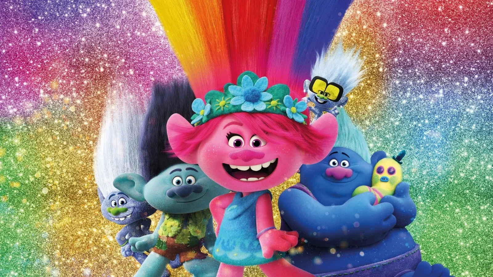 Colourful animated Trolls characters stand smiling in front of a sparkling rainbow background, with the bright pink central Troll wearing a blue dress and flower crown while others with vibrant hair colours and playful expressions gather around her.