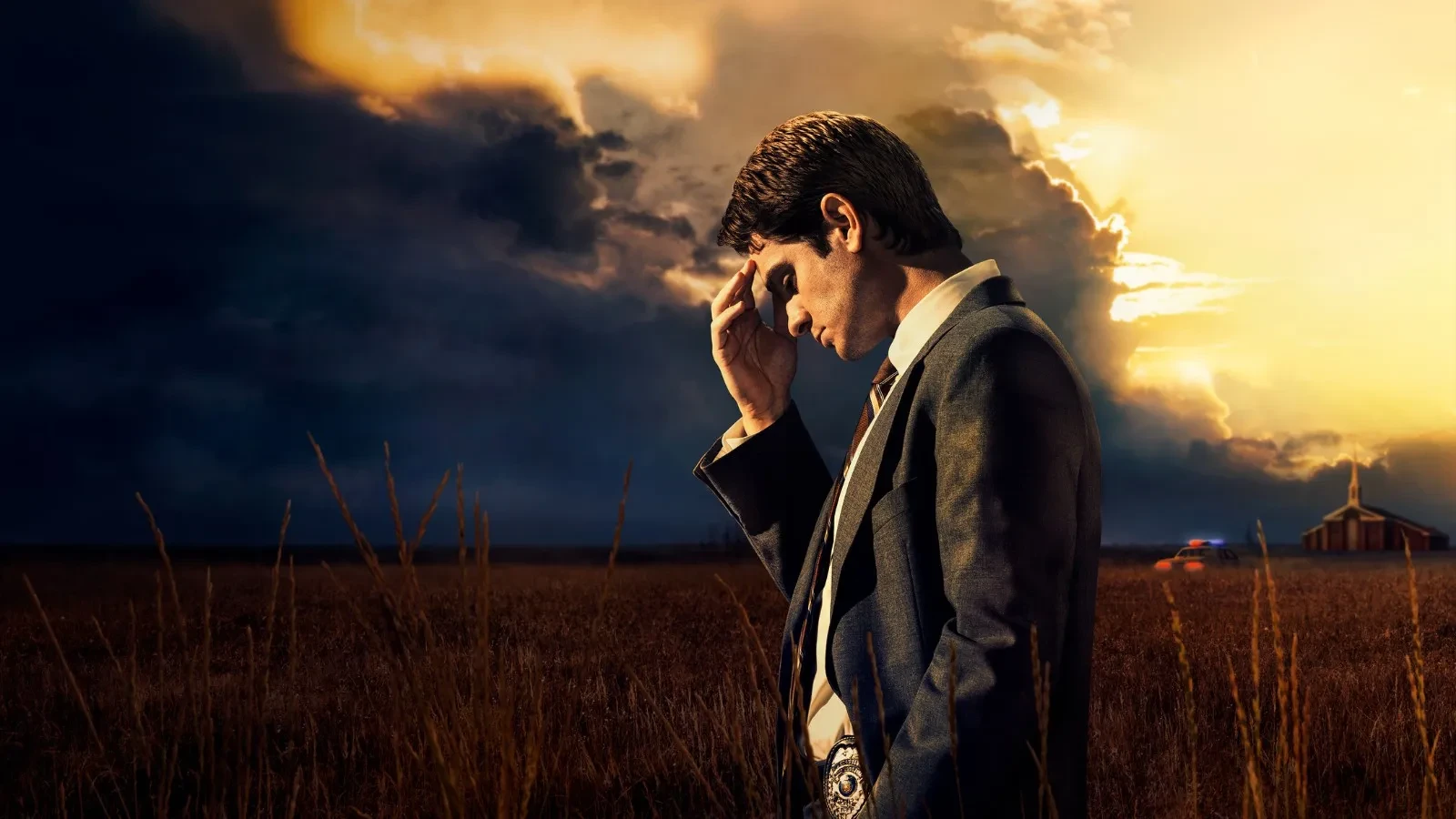 A lone investigator in a suit standing in a vast rural field at sunset, holding a thoughtful pose as dramatic storm clouds gather overhead, with a distant church and police lights illuminating the horizon to create a tense, atmospheric crime‑drama scene.