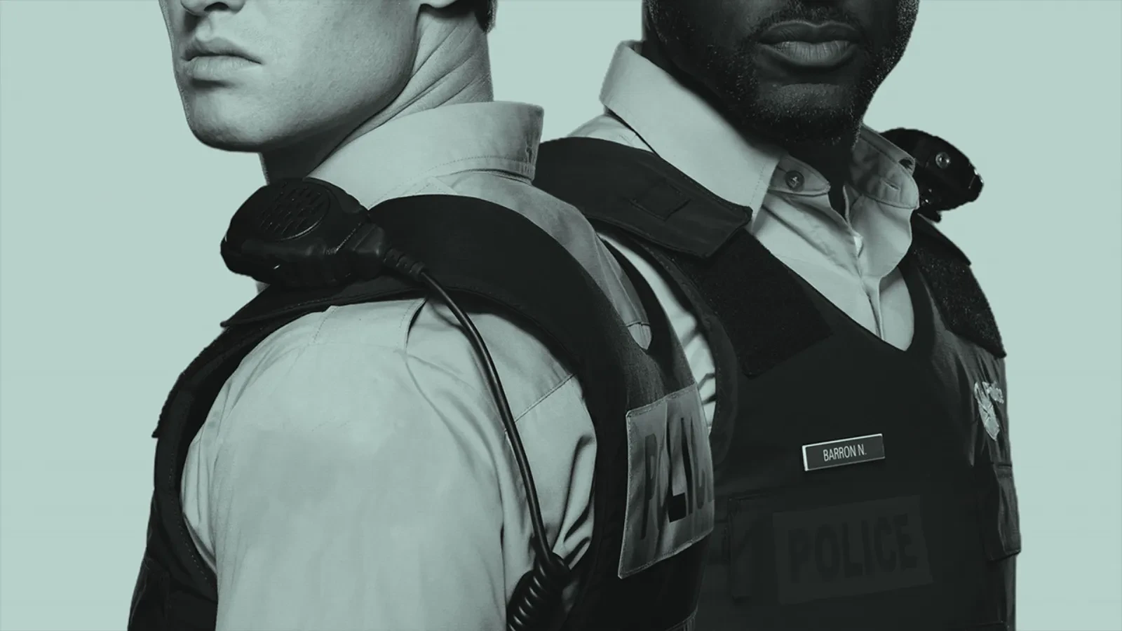 Close-up of two uniformed police officers standing back-to-back, shown from the shoulders to the waist. Both wear tactical vests and radios. One officer’s name tag reads ‘Barron N.’ The image is in a muted, desaturated colour tone. 
