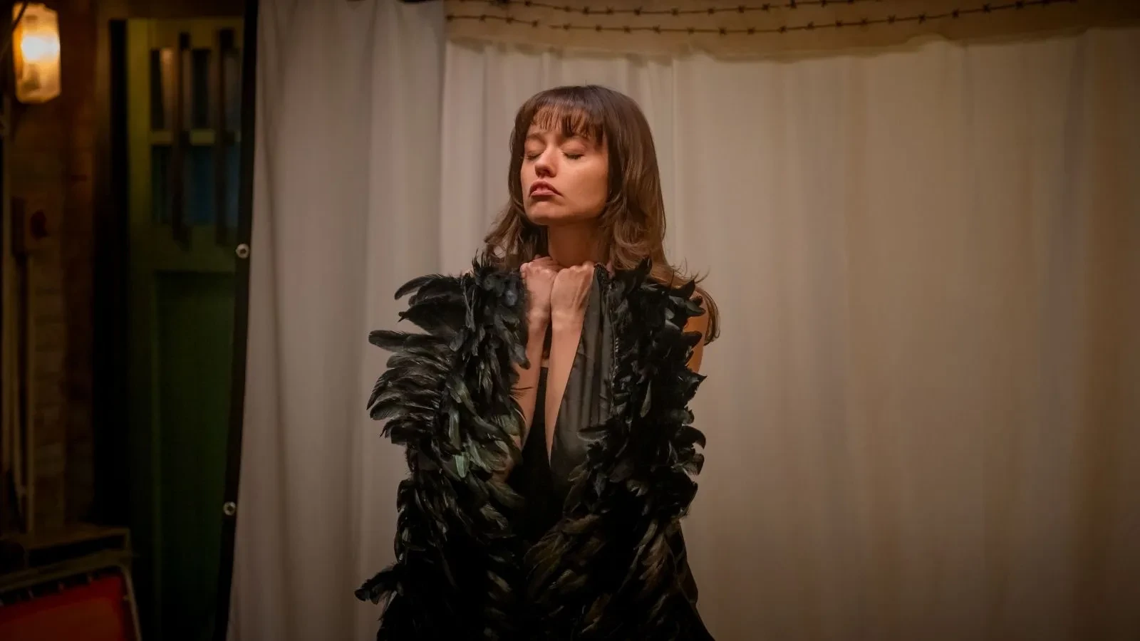 Person dressed in a feathered costume performing on a stage with warm lighting and a curtain backdrop.