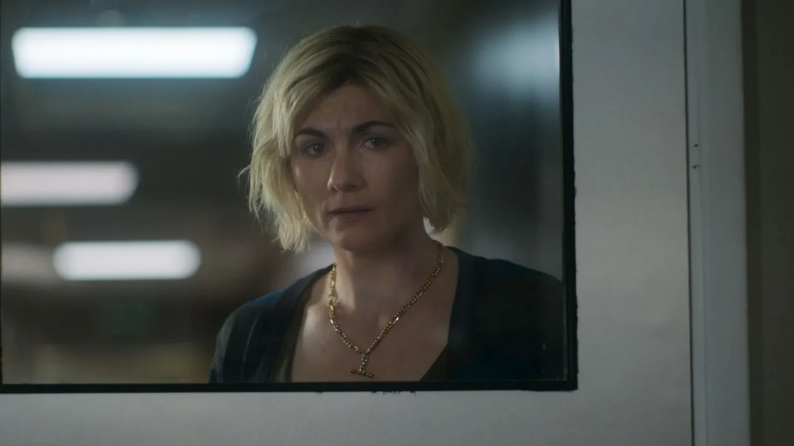 Individual looking through a window panel inside a building hallway with soft overhead lighting.