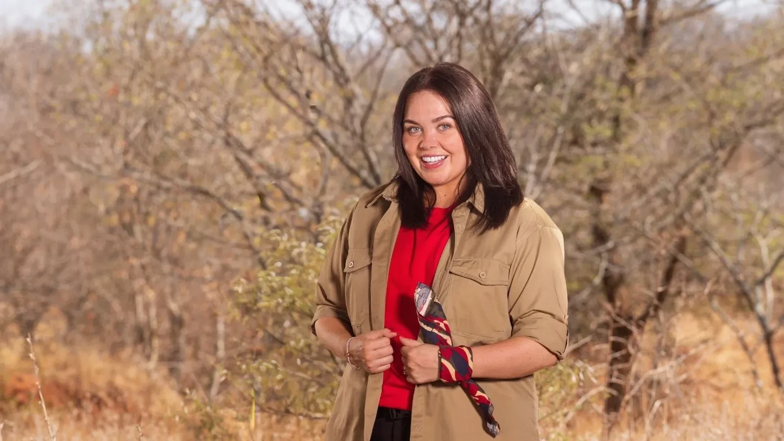 Scarlet Moffat posing in the South African bushland wearing a red top, khaki shirt, and patterned neck scarf.
