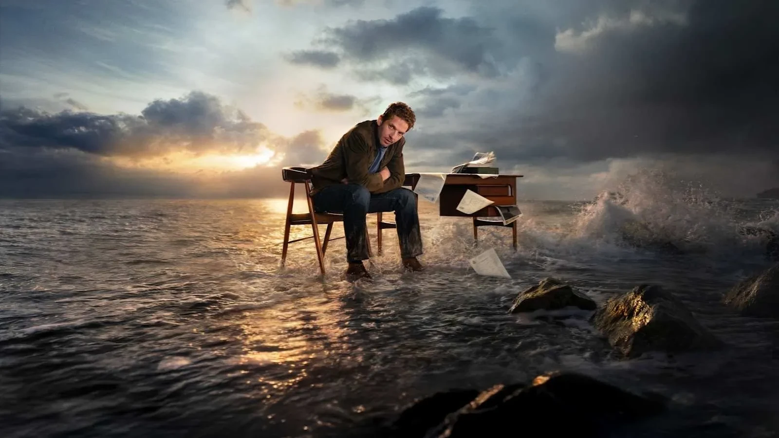 Jim Bergerac sits at a desk surrounded by crashing waves and stormy skies, symbolising inner conflict in the crime drama Bergerac.