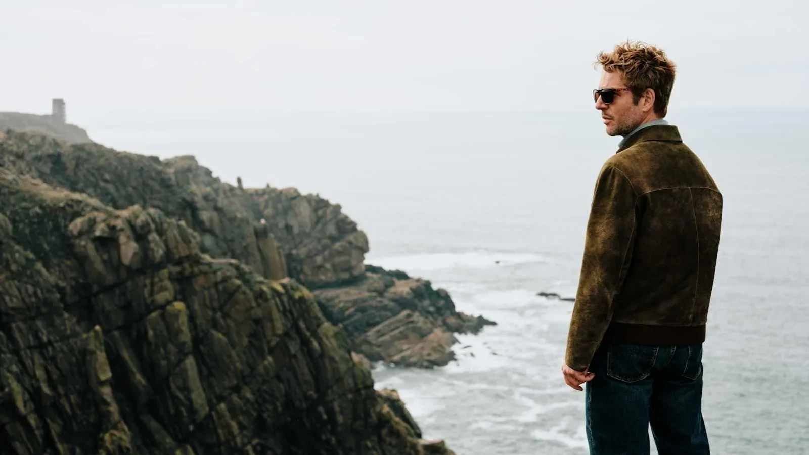 Jim Bergerac stands on rugged coastal cliffs overlooking the sea, capturing the moody Channel Islands setting of the crime drama Bergerac.