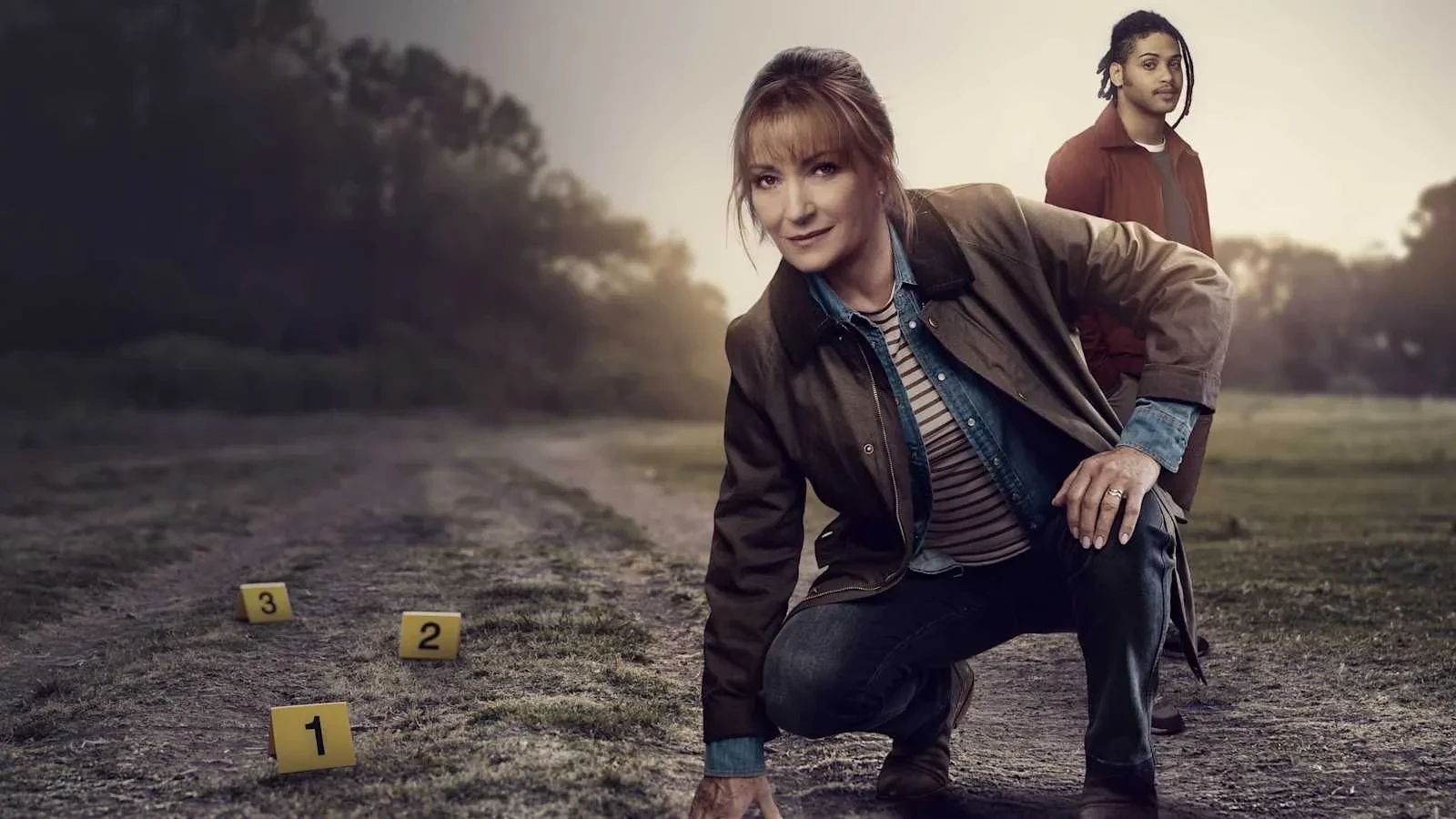 A woman in a hunting style jacket lent down in front of a crime scene with a man in red jacket stood in the background