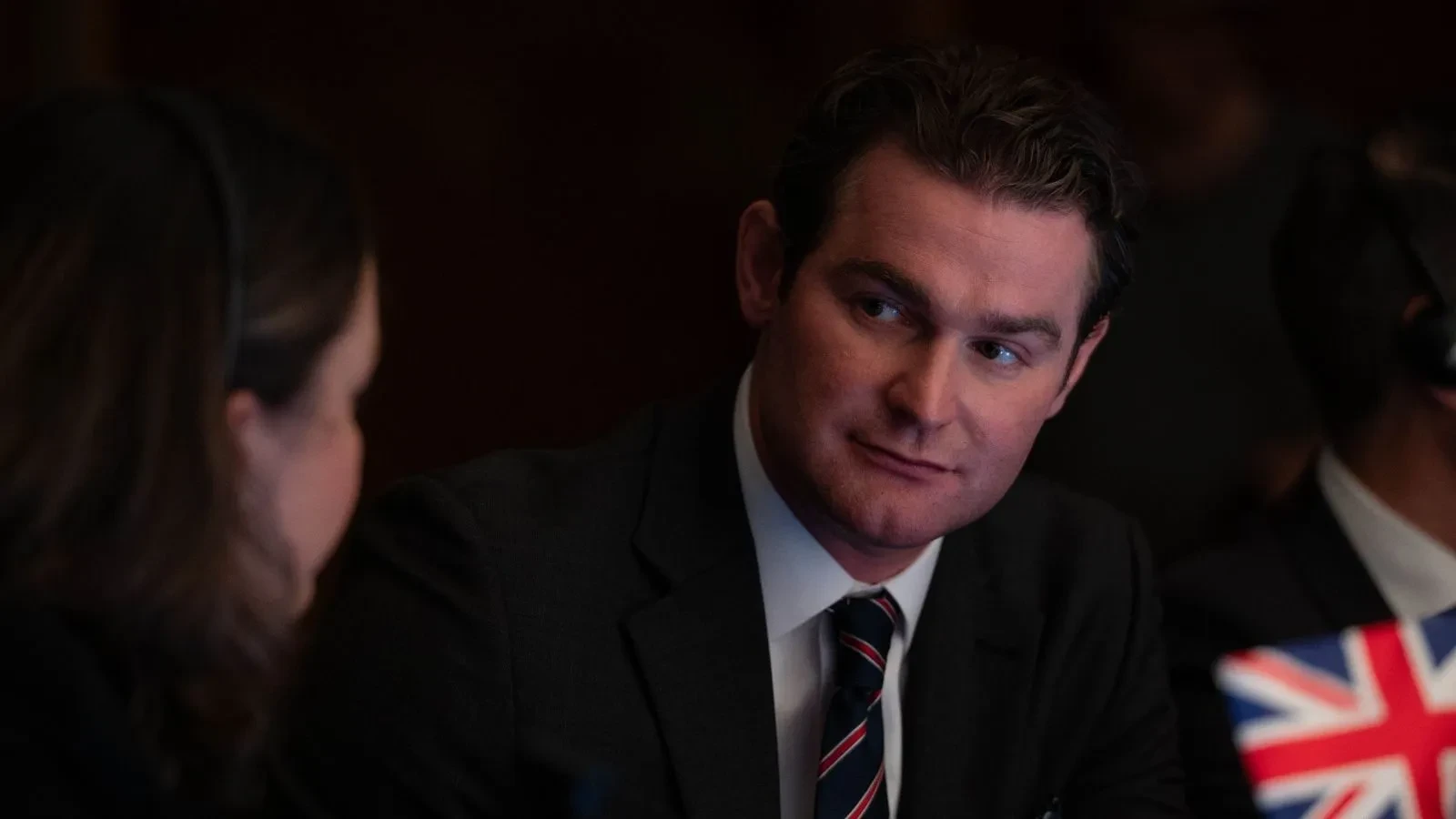 Government official seated at a conference table during a high‑level meeting, shown in a political thriller scene from Secret Service.