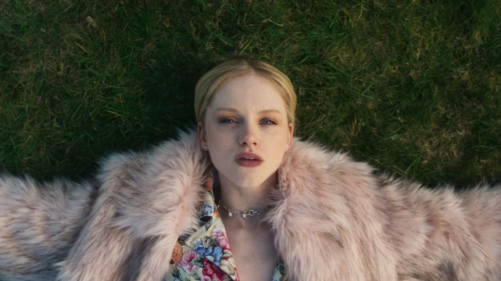 Close-up of two people standing outdoors among tall plants, touching foreheads, with one person’s hand gently placed on the other’s face.