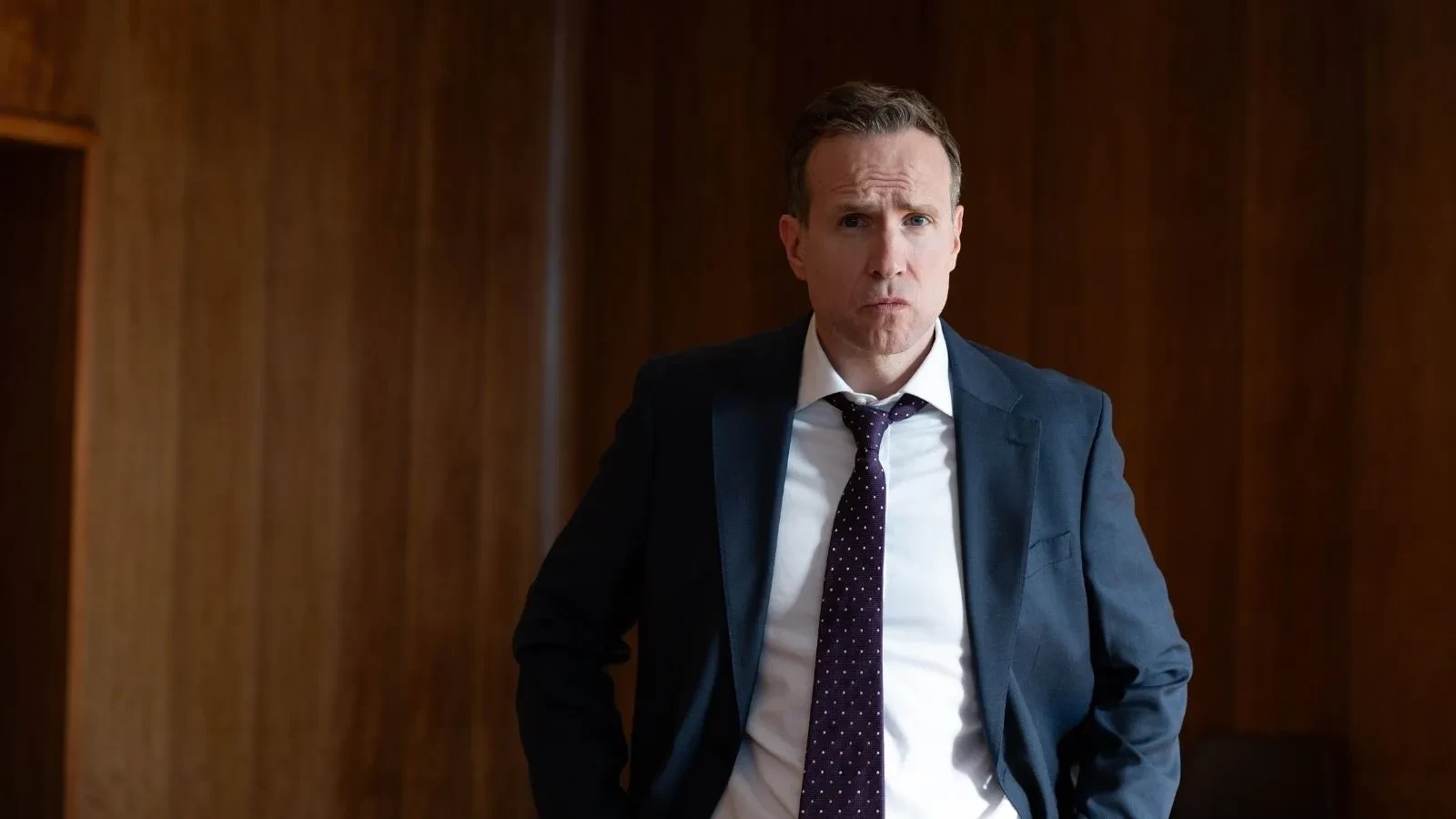 Political figure standing in a formal office setting wearing a suit and tie, from the television drama Secret Service.