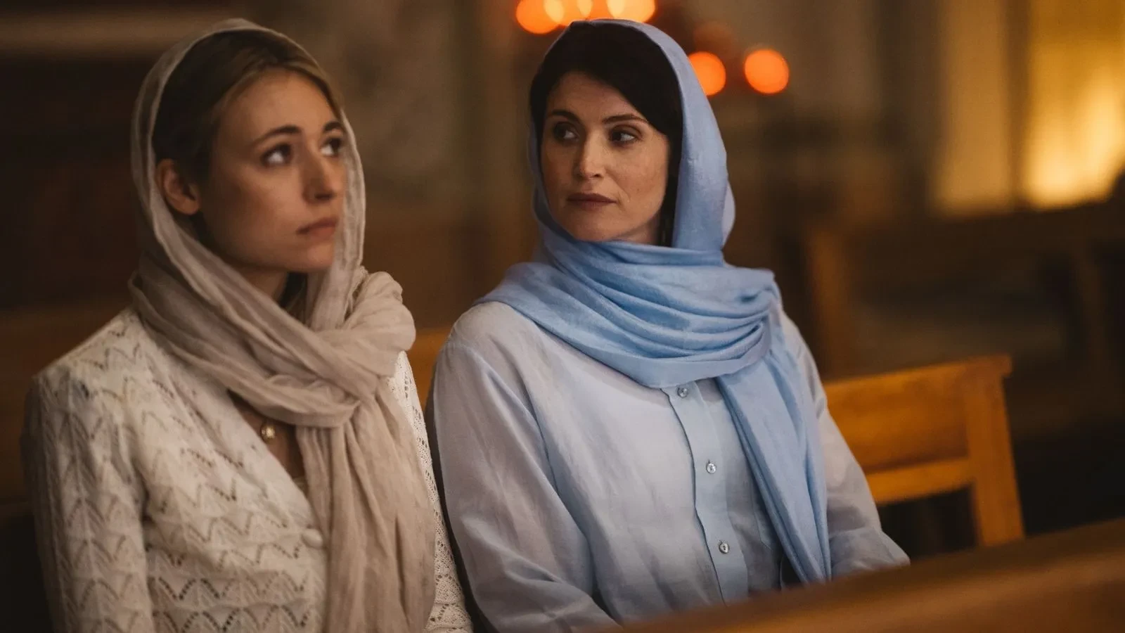 Two women wearing headscarves seated on a wooden bench inside a religious building, shown in Secret Service television series