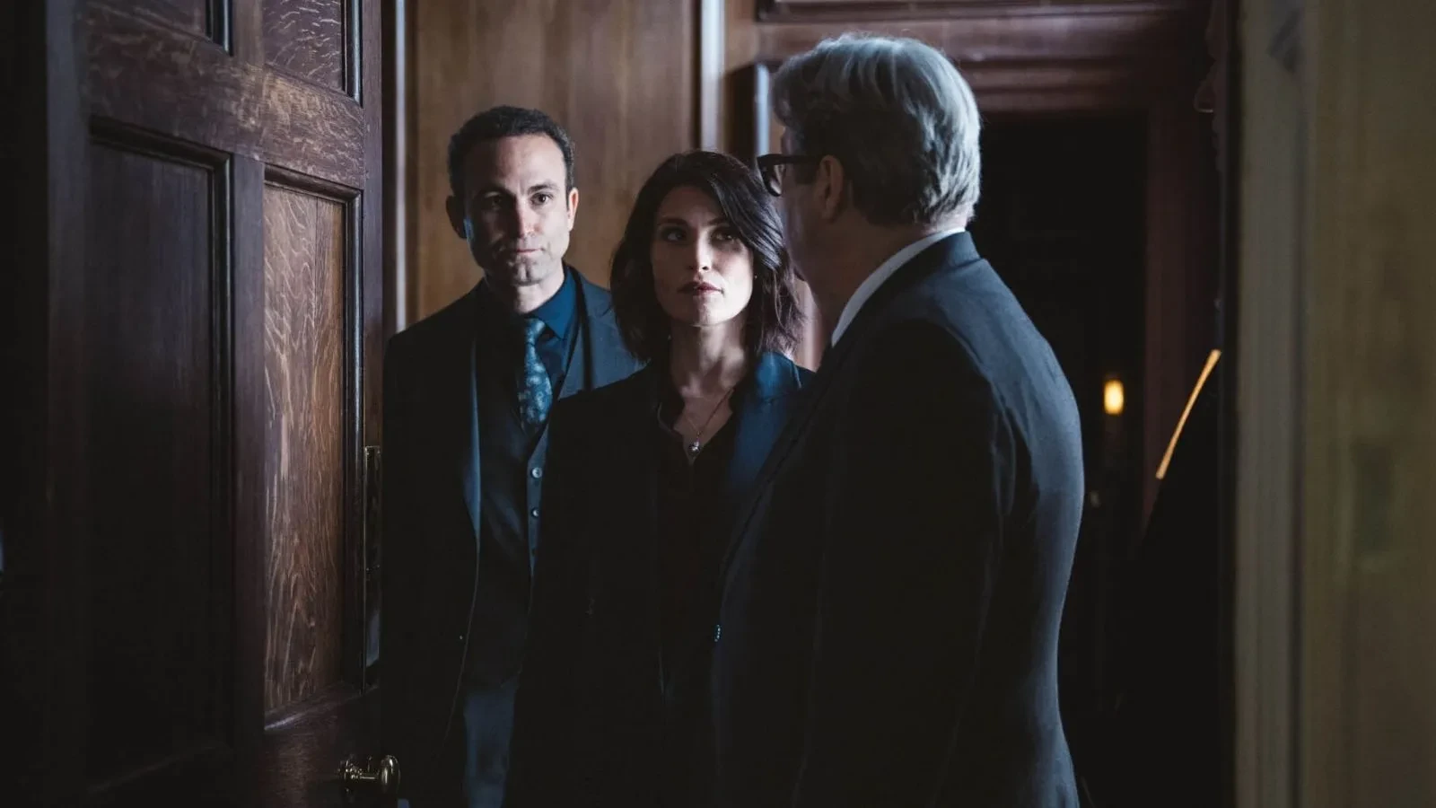 Three intelligence figures standing in a wood-panelled doorway during a serious discussion, scene from the political thriller Secret Service
